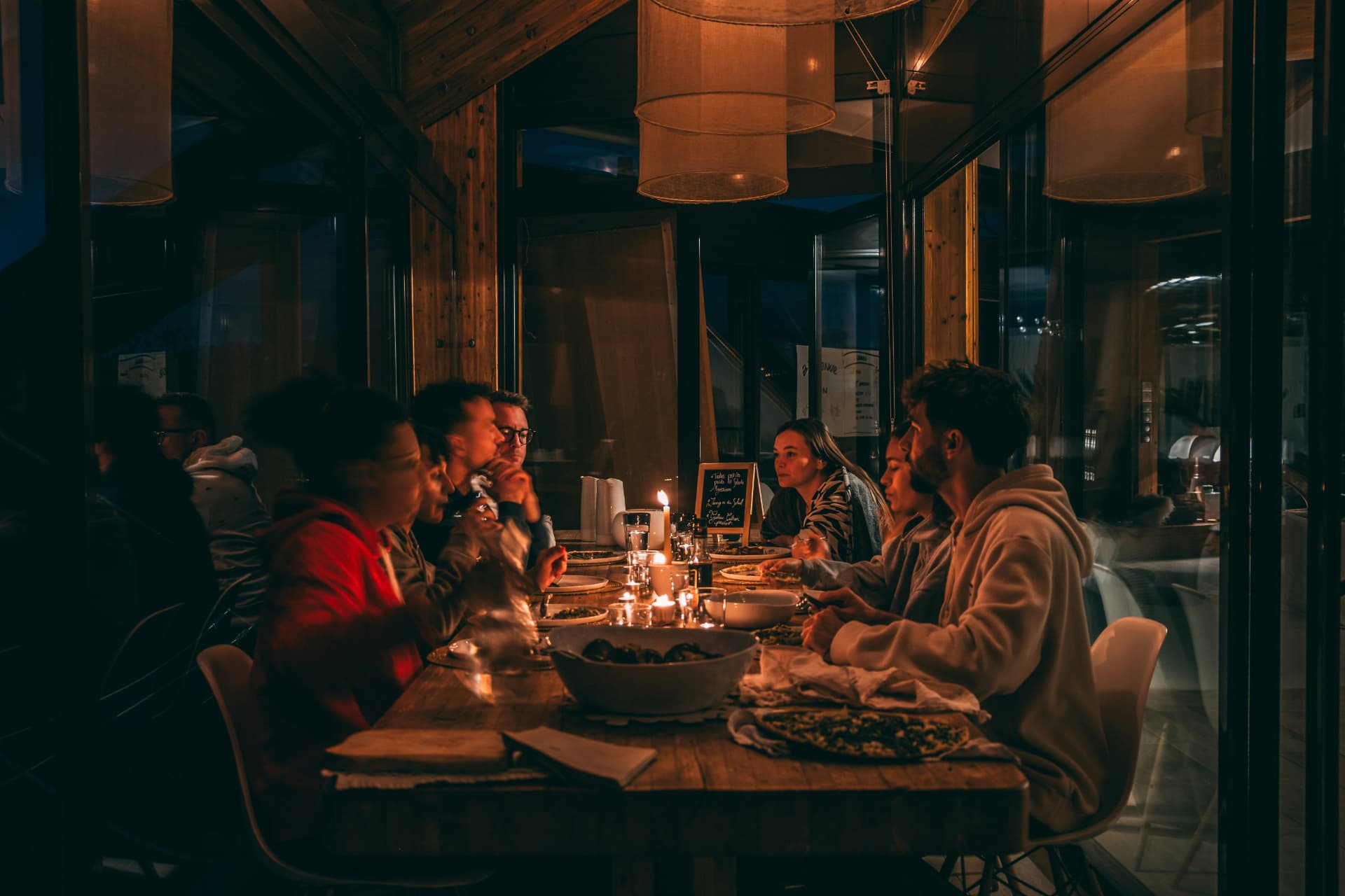 Friends at a long candlelit table sharing food and conversation late at night